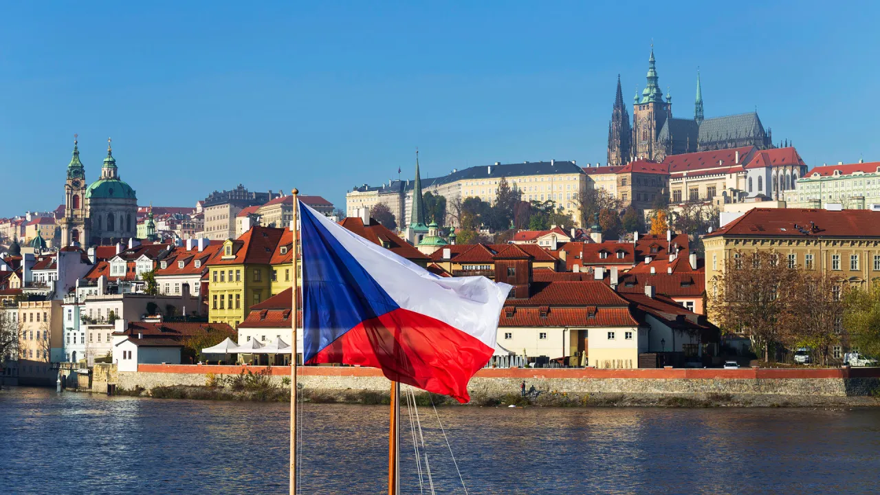 Prague Castle above the Vltava, with the Czech flag in the foreground